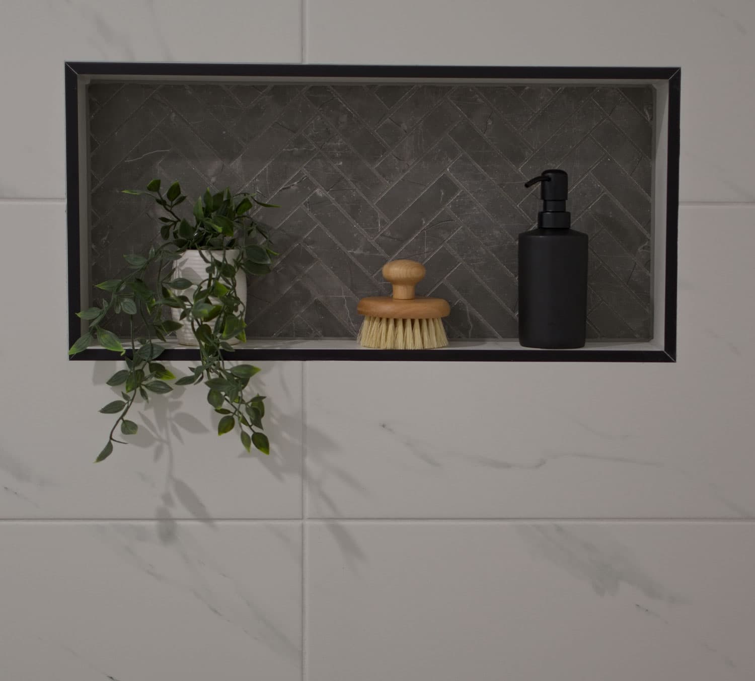 Tiled shower niche with a herringbone stone back and a black trim edge