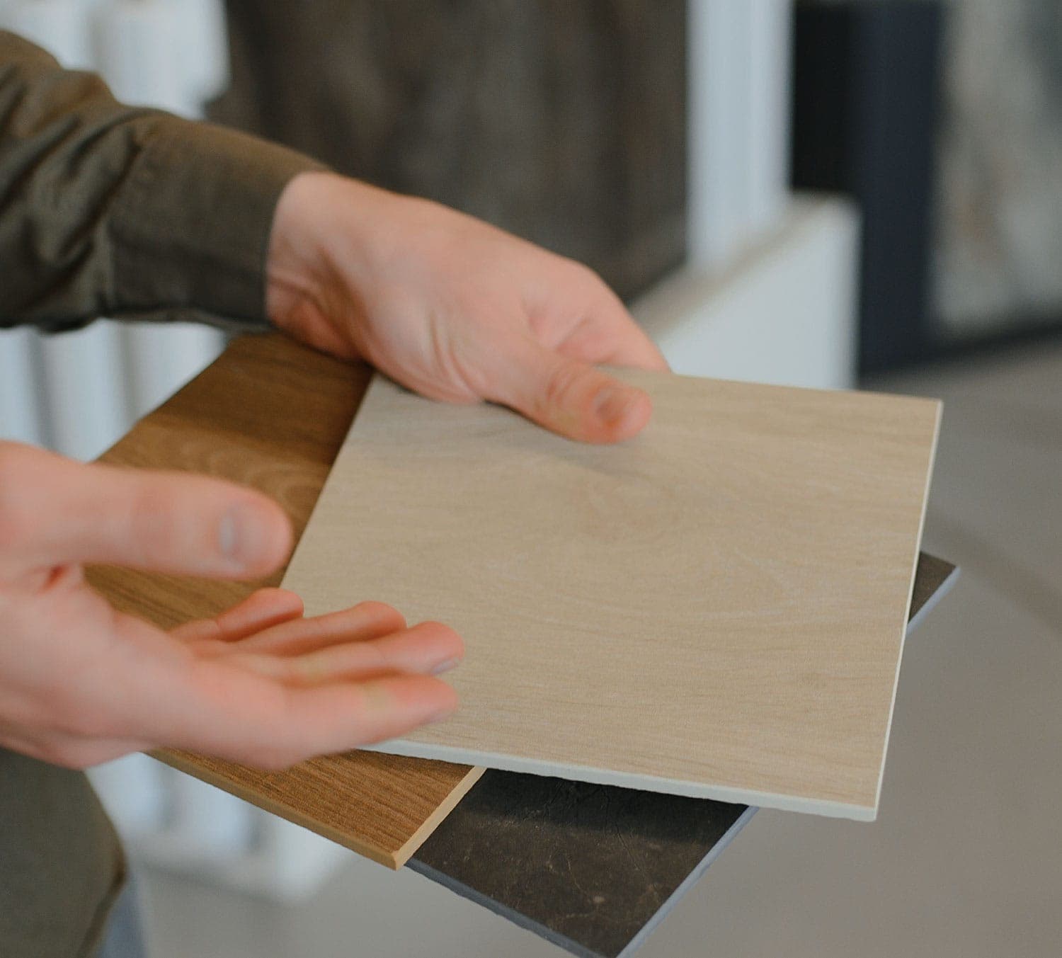 Hands holding timber look and stone look tile samples side by side to compare them