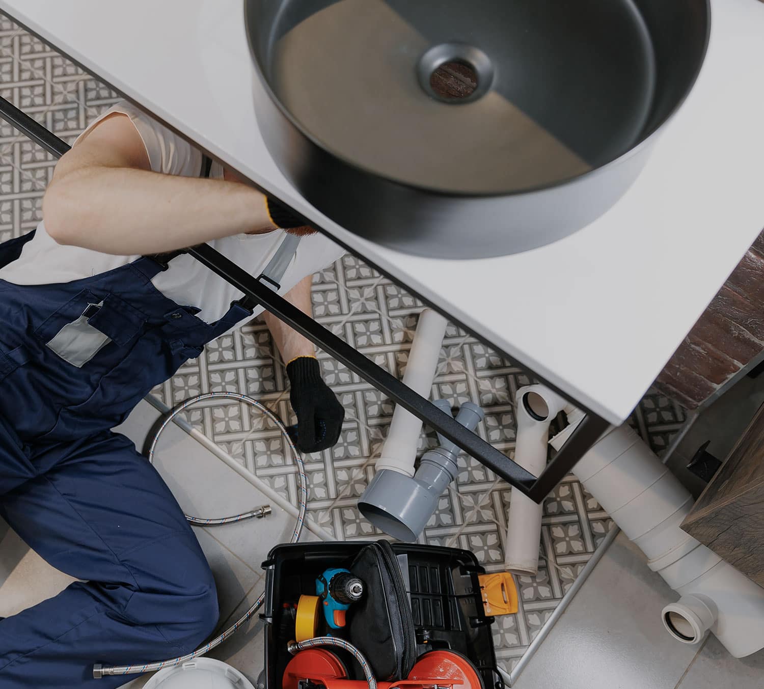 Tradesperson connecting the waste and water lines under a new basin during a bathroom fitout